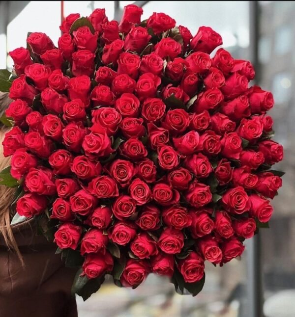 100 Red Roses Grande Bouquet close-up: rows of bright red roses held against a dark background