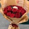 Crimson Heart Bouquet held in hand: red roses with one white rose in brown kraft paper