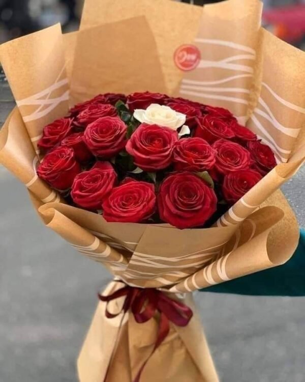 Crimson Heart Bouquet held in hand: red roses with one white rose in brown kraft paper
