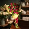 18 Red Roses Bouquet – in a flower shop setting باقة 18 وردة حمراء بورق كرافت موضوعة على طاولة خشبية داخل محل ورد